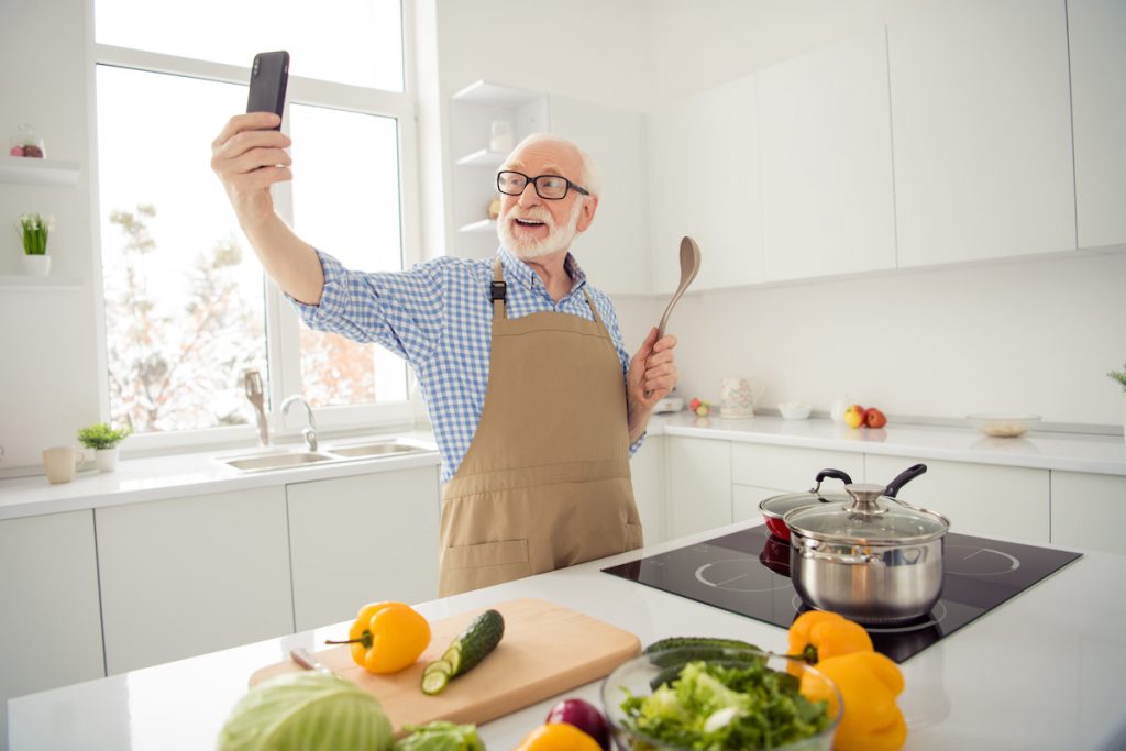 Elderly parent video chatting his caregivers to show that he is safely making food by himself 